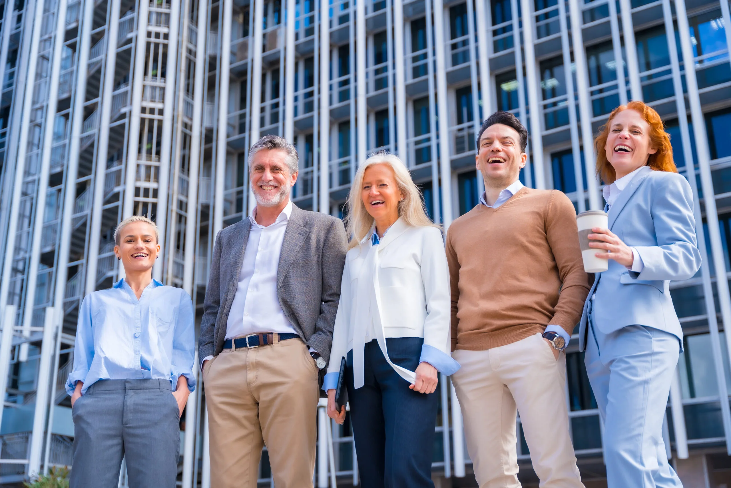 A cheerful group of professional coworkers standing outside a modern office building, representing successful B2B channel partnerships.